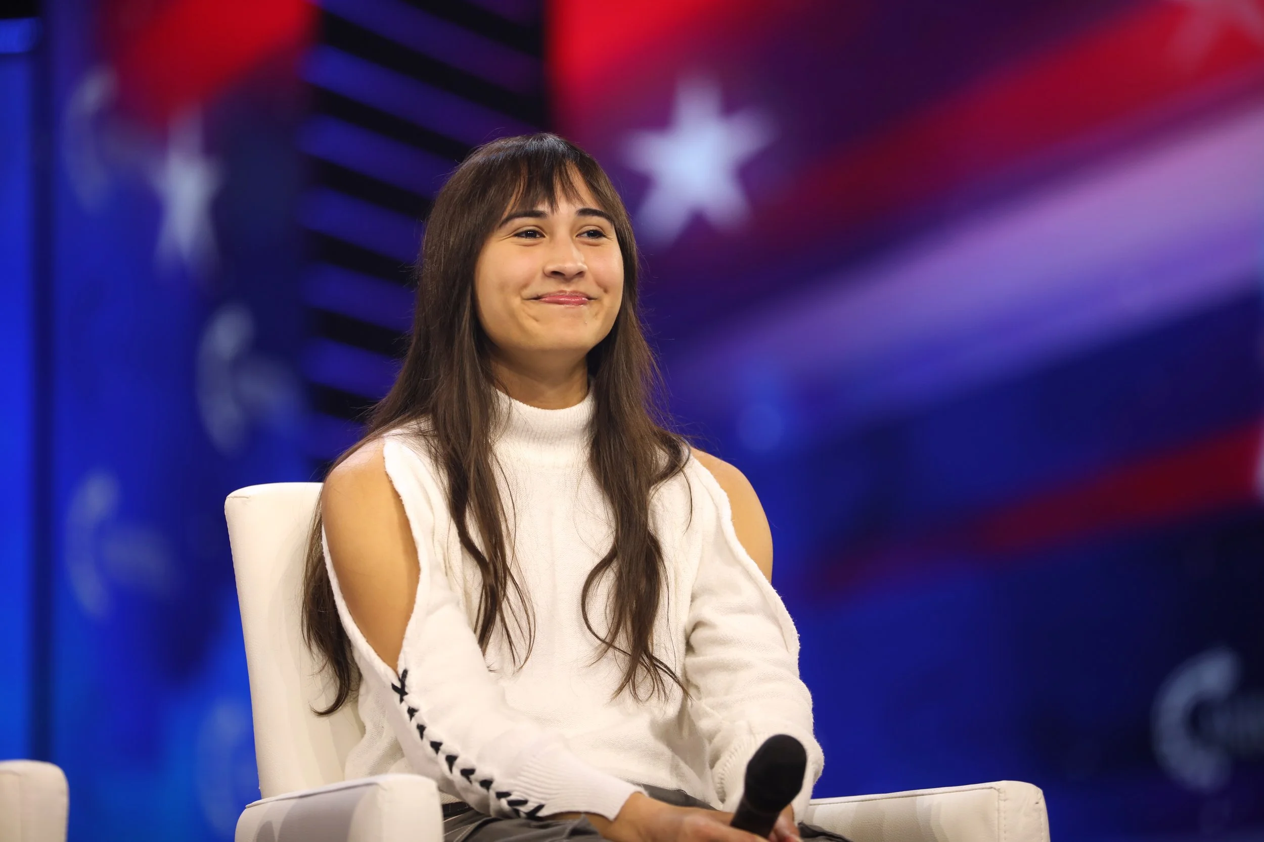 Chloe Cole seated on stage with a microphone